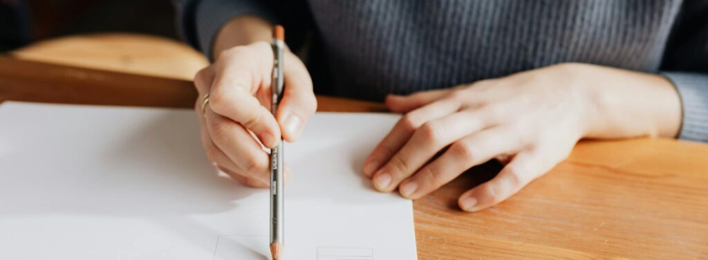 Person sketching on white paper with pencil on a wooden table, showcasing artistic creativity.
